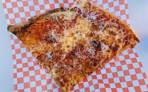 A New York-style pizza slice on a checkered paper plate